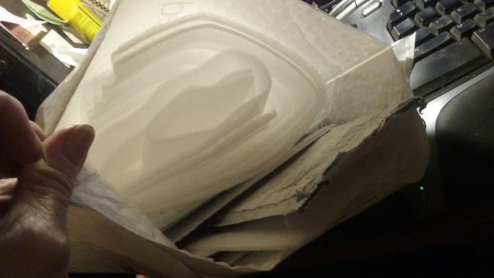 Eine Hand h&auml;lt Luftpolsterfolie, die teilweise entrollt ist, w&auml;hrend sie auf einem Tisch neben einer computergest&uuml;tzten Arbeitsfl&auml;che liegt.