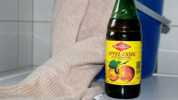 Ein Essigflasche steht neben einem ausgeleierten Wollpullover auf einem Tisch, bereit zum Formen mit Essigwasser.