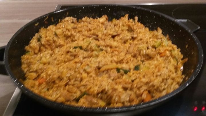 Eine gro&szlig;e Pfanne mit einer goldbraunen Gyros-Reispfanne, die auf einem Herd steht und dampft.