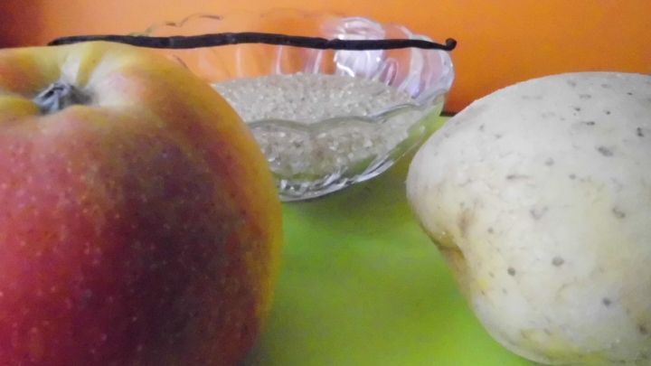 Ein roter Apfel und eine Birne liegen auf einer gr&uuml;nen Oberfl&auml;che, daneben steht eine Sch&uuml;ssel. Die Wand ist orange.