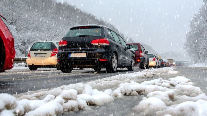 Schwarzes Auto f&auml;hrt vorsichtig auf einer schneebedeckten Stra&szlig;e, umgeben von anderen Fahrzeugen und fallendem Schnee.