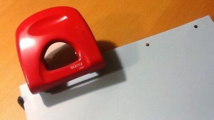 Ein roter Locher stanzt L&ouml;cher in ein Blatt Papier, das auf einem Holzschreibtisch liegt.