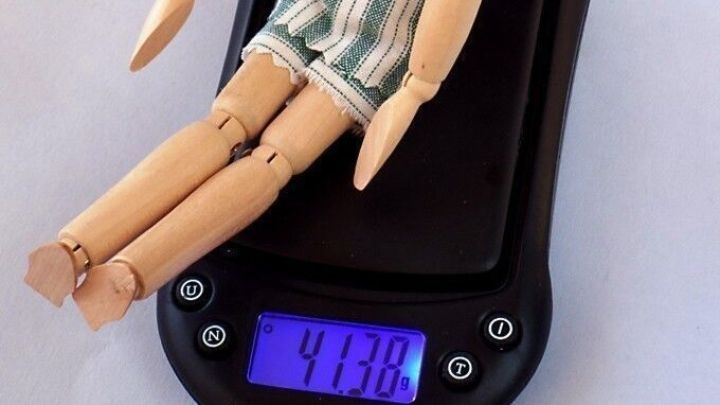 Eine Holzpuppe sitzt auf einer digitalen Waage und zeigt 41,38 an, als Teil einer Ern&auml;hrungsumstellung.