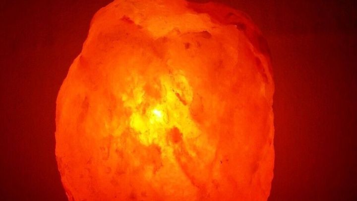 Eine Salzkristalllampe leuchtet sanft rot auf einem Tisch im Schlafzimmer und schafft eine entspannende Atmosph&auml;re.