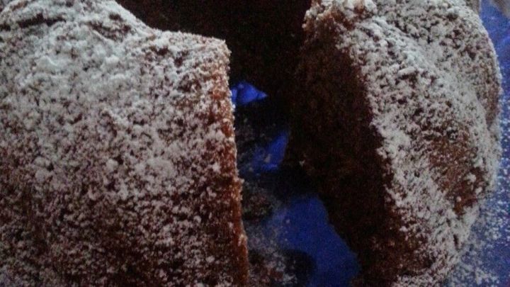 Ein schokoladiger Bundt-Kuchen steht auf einem blauen Teller, mit Puderzucker best&auml;ubt und teils angeschnitten.