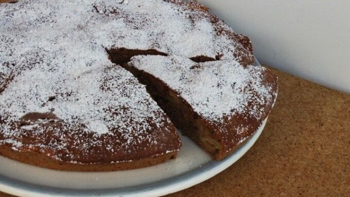 Eine Apfeltarte liegt auf einem Teller, mit Puderzucker best&auml;ubt und teilweise angeschnitten, auf einem Holzuntergrund.