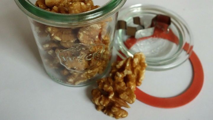 Ein Glas mit Waln&uuml;ssen steht offen, einige N&uuml;sse liegen daneben. Der Hintergrund ist neutral und hell.