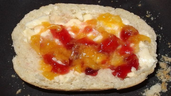 Ein Br&ouml;tchen ist auf einer Pfanne platziert, belegt mit buntem Orangenmark und Marmelade, um einen Snack zu kreieren.
