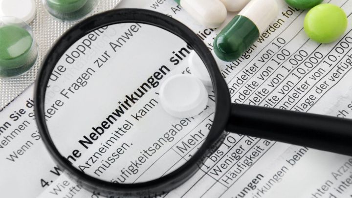 Wei&szlig;tabletten und Kapseln liegen neben einem Dokument, auf dem "Nebenwirkungen" unter einer Lupe deutlich zu erkennen sind.
