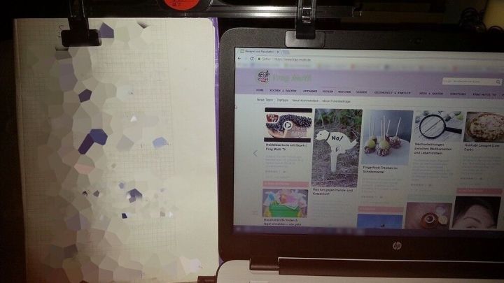 Ein Laptop steht neben einem wei&szlig;en Blatt Papier, das fixiert ist; der Laptop zeigt eine Webseite mit verschiedenen Inhalten.