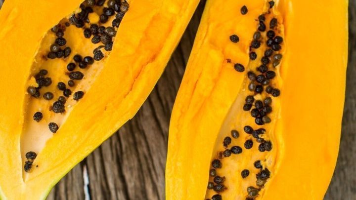 Zwei halbierte Papayas liegen auf einem Holztisch, die orangefarbene Frucht zeigt ihre schwarzen Samen im Inneren.