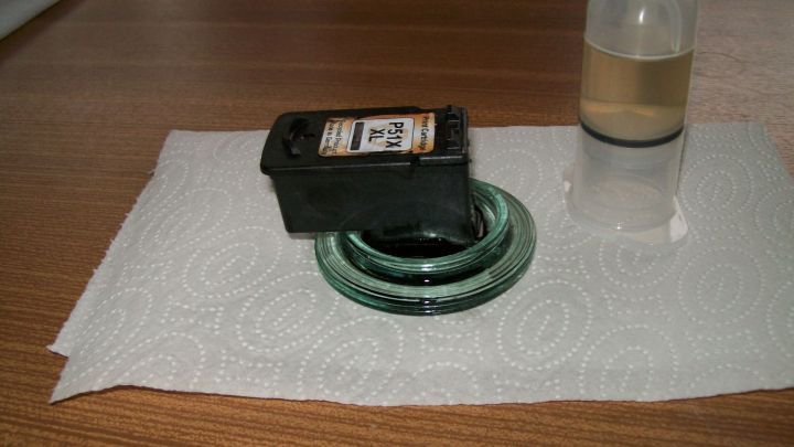 Die Druckerpatrone liegt auf einem Papiertuch, w&auml;hrend ein Reinigungsmittel in einem Fl&auml;schchen daneben steht.