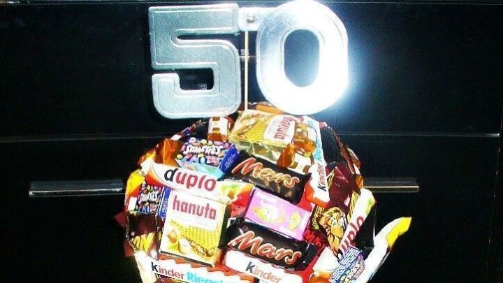 Ein bunter S&uuml;&szlig;igkeitenbaum aus verschiedenen Schokoladen ist auf einem Eimer mit Kies montiert, dekoriert f&uuml;r einen Anlass.