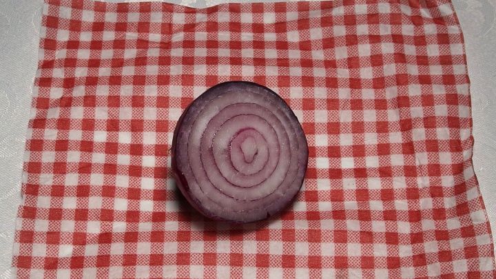 Ein roter Zwiebelsack liegt auf einem karierten Tuch, bereit zur Anwendung bei Ohrenschmerzen.