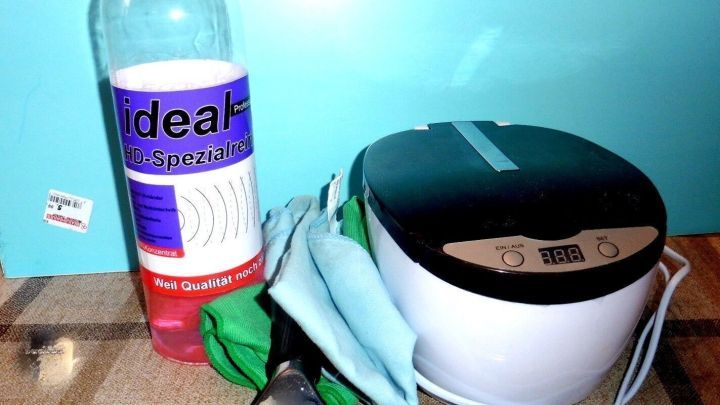 Eine Flasche Reiniger steht neben einem Dampfreiniger und Reinigungst&uuml;chern auf einem Holzuntergrund zum Fensterreinigung.