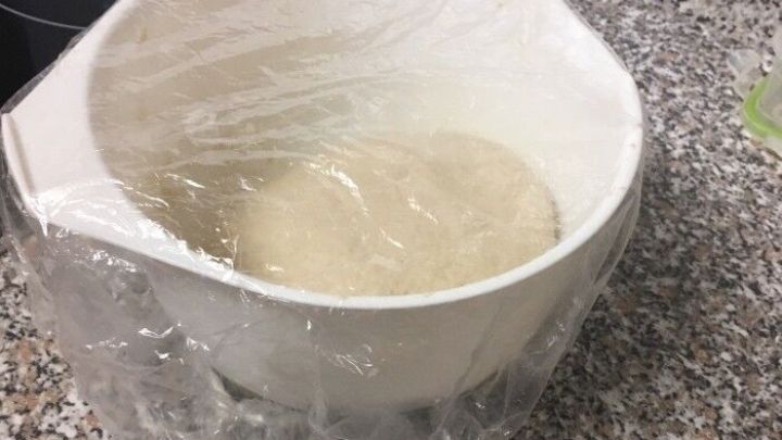 Ein R&uuml;hrsch&uuml;ssel mit Hefeteig ist mit Frischhaltefolie abgedeckt und steht auf einer K&uuml;chentheke aus Granit.