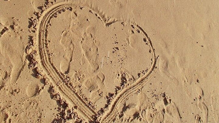 Ein Herz ist im Sand gezeichnet, w&auml;hrend die Wellen sanft an den Strand sp&uuml;len. Perfekt f&uuml;r einen Strandurlaub.
