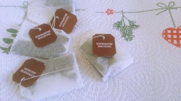 Schwarzteebeutel liegen auf einer Tischdecke mit Pflanzenmotiven, bereit f&uuml;r den Einsatz im Garten zur Verbesserung des Bodens.