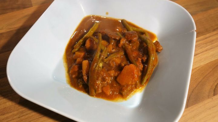 Lamm-Curry mit Bohnen und S&uuml;&szlig;kartoffeln in einer wei&szlig;en Sch&uuml;ssel, k&ouml;stlich angerichtet auf einem Holzuntergrund.