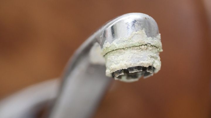 Ein Wasserhahn hat Ablagerungen und Kalkreste am Auslauf, was auf die Notwendigkeit des Entkalkens hinweist.