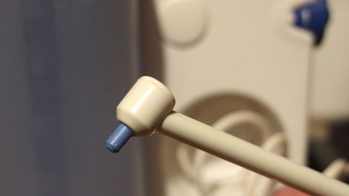 Ein kleiner, wei&szlig;er Ohrst&ouml;psel wird von einer Hand gehalten, w&auml;hrend er vor einem Ger&auml;tschaften-Hintergrund positioniert ist.