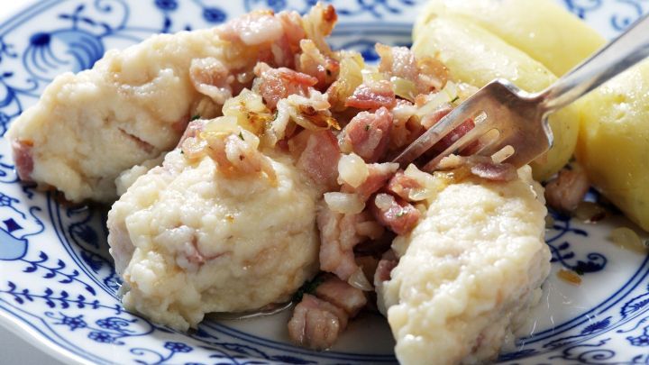 Eine zarte, warme Geheiratet-Portion auf einem blauen Teller, belegt mit knusprigen Zwiebeln und Speck, daneben Kartoffeln.