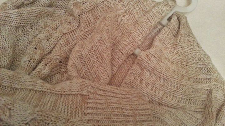 Ein beiger, eingeknickter Pulli h&auml;ngt an einem Kleiderb&uuml;gel, bereit zu entspannen oder gefaltet zu werden.
