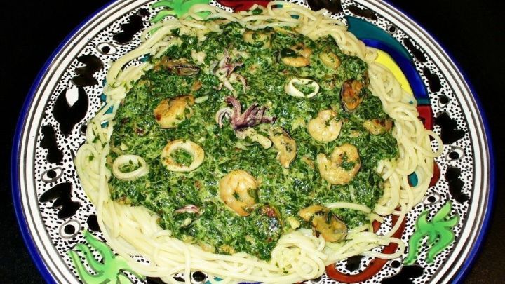 Spaghetti sind mit einer gr&uuml;nen Spinatsauce und Meeresfr&uuml;chten auf einem bunten Teller angerichtet, vor schwarzem Hintergrund.