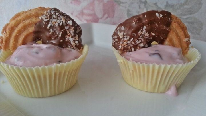 Zwei Schokoladen-Dessert-Sch&auml;lchen stehen auf einem wei&szlig;en Teller, gef&uuml;llt mit rosa Creme und dekoriert mit Keksen.