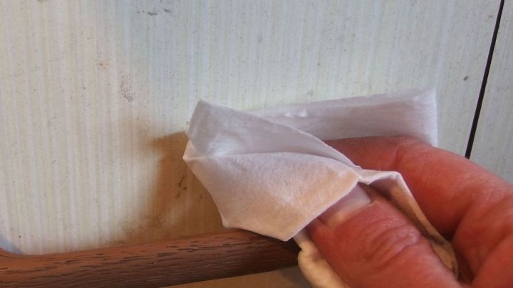 Eine Hand wischt mit einem Feuchttuch einen Fleck von einer hellen Wand neben einem Holzgriff.