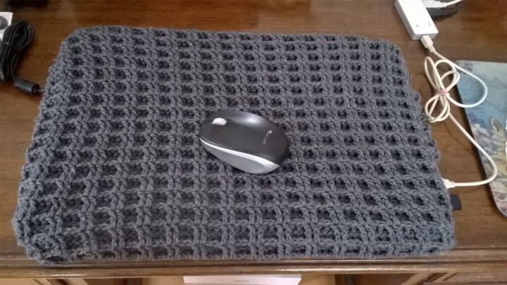 Eine graue Laptop-Abdeckung liegt auf einem Tisch und ein Computer-Maus steht darauf, umgeben von Kabeln und Holzoberfl&auml;che.