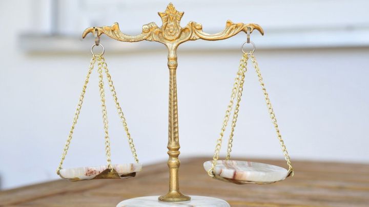 Eine goldene Waage steht stabil auf einem h&ouml;lzernen Tisch und balanciert gleichm&auml;&szlig;ige Gewichte in einem hellen Raum.