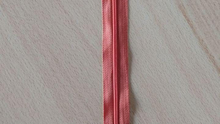 Der Rei&szlig;verschluss liegt auf einer Holzoberfl&auml;che und zeigt eine Bandh&auml;lfte, die offen und einsam wirkt.