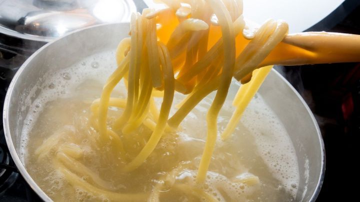 Eine Gabel hebt gekochte Nudeln aus einem sprudelnden Wasserkochtopf, um sie zum Abtropfen zu entnehmen.