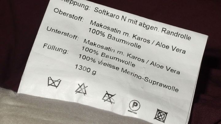 Ein Pflegeetikett zeigt Anweisungen wie "nicht waschen" und Materialhinweise f&uuml;r Textilien in einem Schlafzimmer.