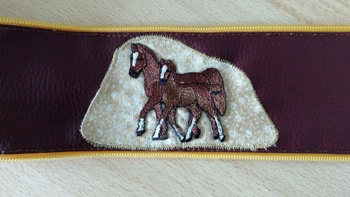 Ein braunes Pferdemotiv ist auf einer Vlieseline mit purpurfarbenem Kunstleder platziert, was eine kreative Dekoration darstellt.