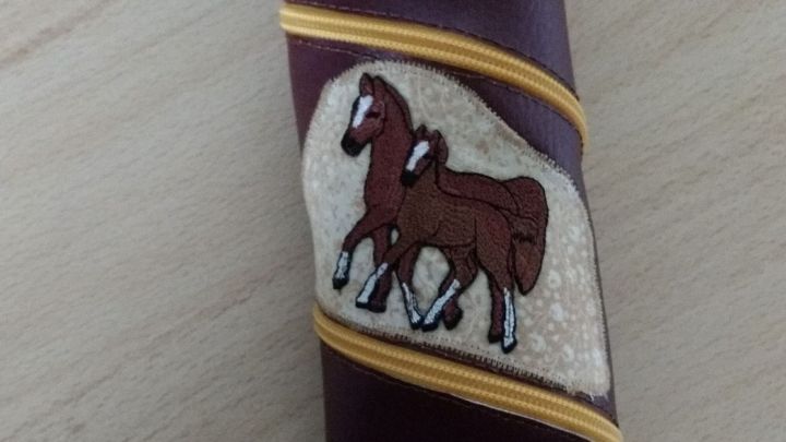 Ein spiralf&ouml;rmiges M&auml;ppchen aus Kunstleder mit einem Pferdemotiv steht auf einem Tisch aus Holz.