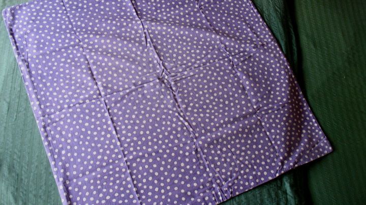 Ein standardm&auml;&szlig;iger Bezug liegt flach auf einem gr&uuml;nen Untergrund, bereit f&uuml;r kleinere Kopfkissen. Das Design ist lila mit wei&szlig;en Punkten.