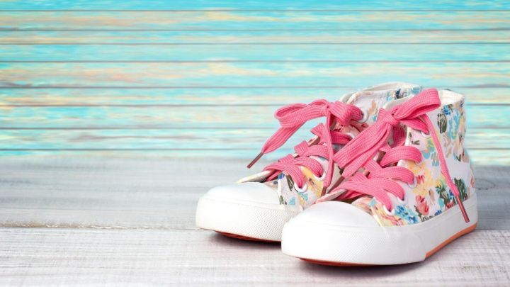 Bunte Sneaker mit rosa Schn&uuml;rsenkeln stehen auf einem hellen Holzuntergrund vor einer pastellfarbenen Wand.