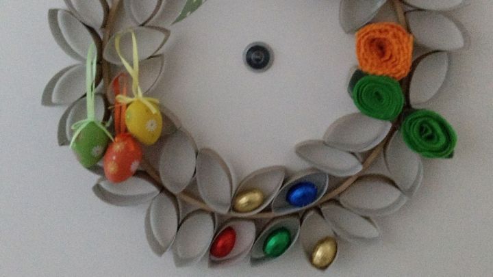 Ein dekorativer Osterkranz h&auml;ngt an der T&uuml;r, geschm&uuml;ckt mit bunten Eiern und einem gr&uuml;nen, gepunkteten Band.