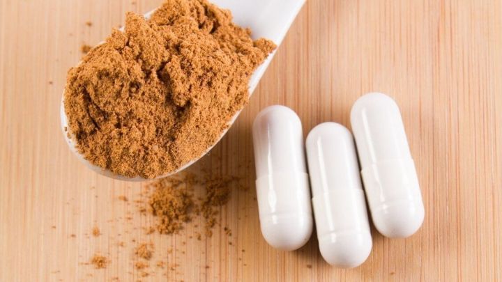 Eine Schaufel Guarana-Pulver liegt neben drei wei&szlig;en Kapseln auf einer Holzoberfl&auml;che, bereit zur Anwendung gegen Kater.