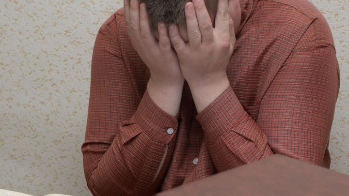 Ein gestresster Student sitzt an einem Tisch, h&auml;lt seinen Kopf in den H&auml;nden und um ihn herum liegen zahlreiche B&uuml;cher, w&auml;hrend er sich auf die Pr&uuml;fungszeit konzentrieren m&ouml;chte.