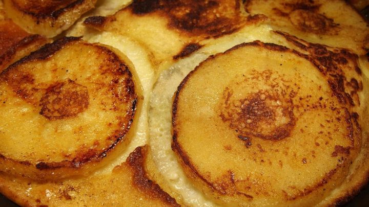 Luftige Pfannkuchen mit gebratenen Apfelscheiben liegen goldbraun in einer Pfanne, umgeben von einem zarten Teig.