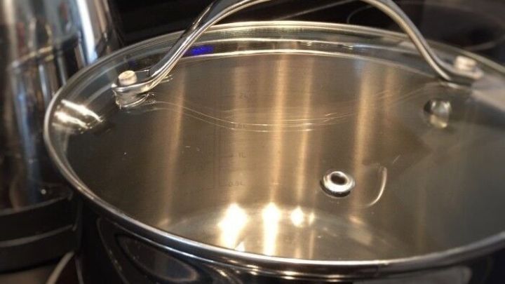 Ein silberner Topfdeckel liegt auf einem schwarzen Herd, w&auml;hrend ein Wasserkocher daneben steht, was beim Stromsparen hilft.