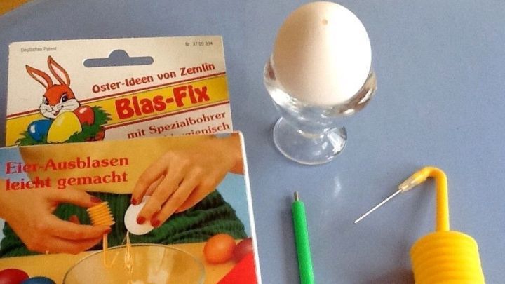Ein Ei steht auf einem Eierbecher, umgeben von einem Blasger&auml;t und einer Anleitung f&uuml;r das einfache Eier Ausblasen.