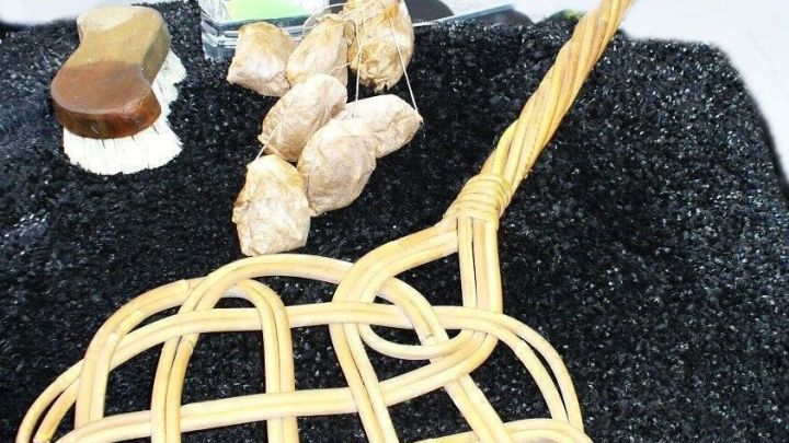 Ein geflochtener Sieb aus Weide steht auf einem schwarzen Teppich und umgeben von Wasserflasche und Muscheln.