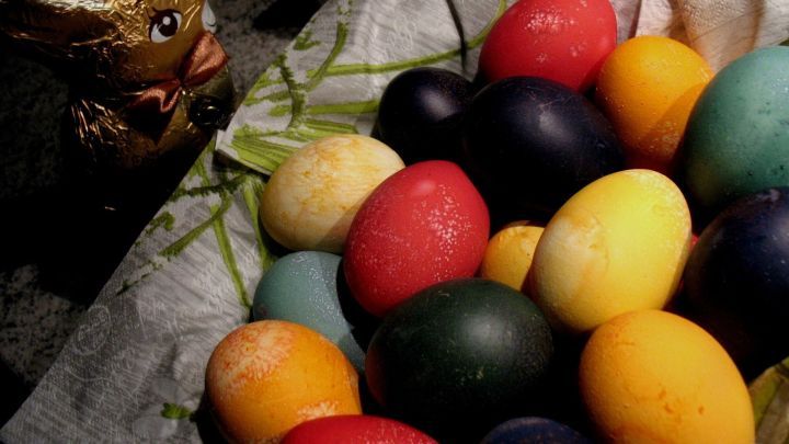 Bunte Ostereier liegen auf einer Serviette und umgeben von einem Hasen-Fig&uuml;rchen in einer festlichen Umgebung.