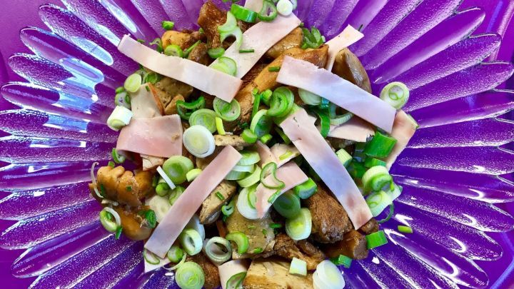 Ein bunter Salat aus Pfifferlingen und Steinpilzen liegt ansprechend auf einem lila Teller, garniert mit Fr&uuml;hlingszwiebeln.