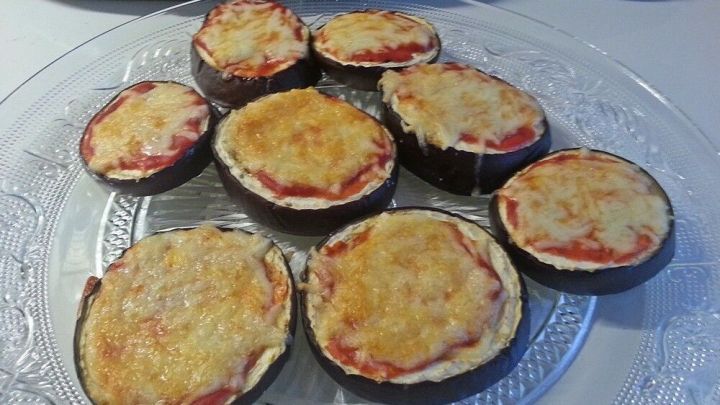 Kleine Auberginen-Pizzen liegen auf einem Glasservierplatte, &uuml;berbacken mit K&auml;se und Tomatensauce, daneben liegt eine Zucchini.