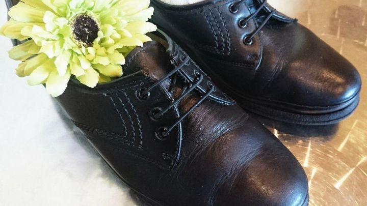 Schwarze Schn&uuml;rschuhe stehen neben einer hellen Bl&uuml;te auf einer gl&auml;nzenden Oberfl&auml;che, bereit f&uuml;r die Umwandlung in Slipper.